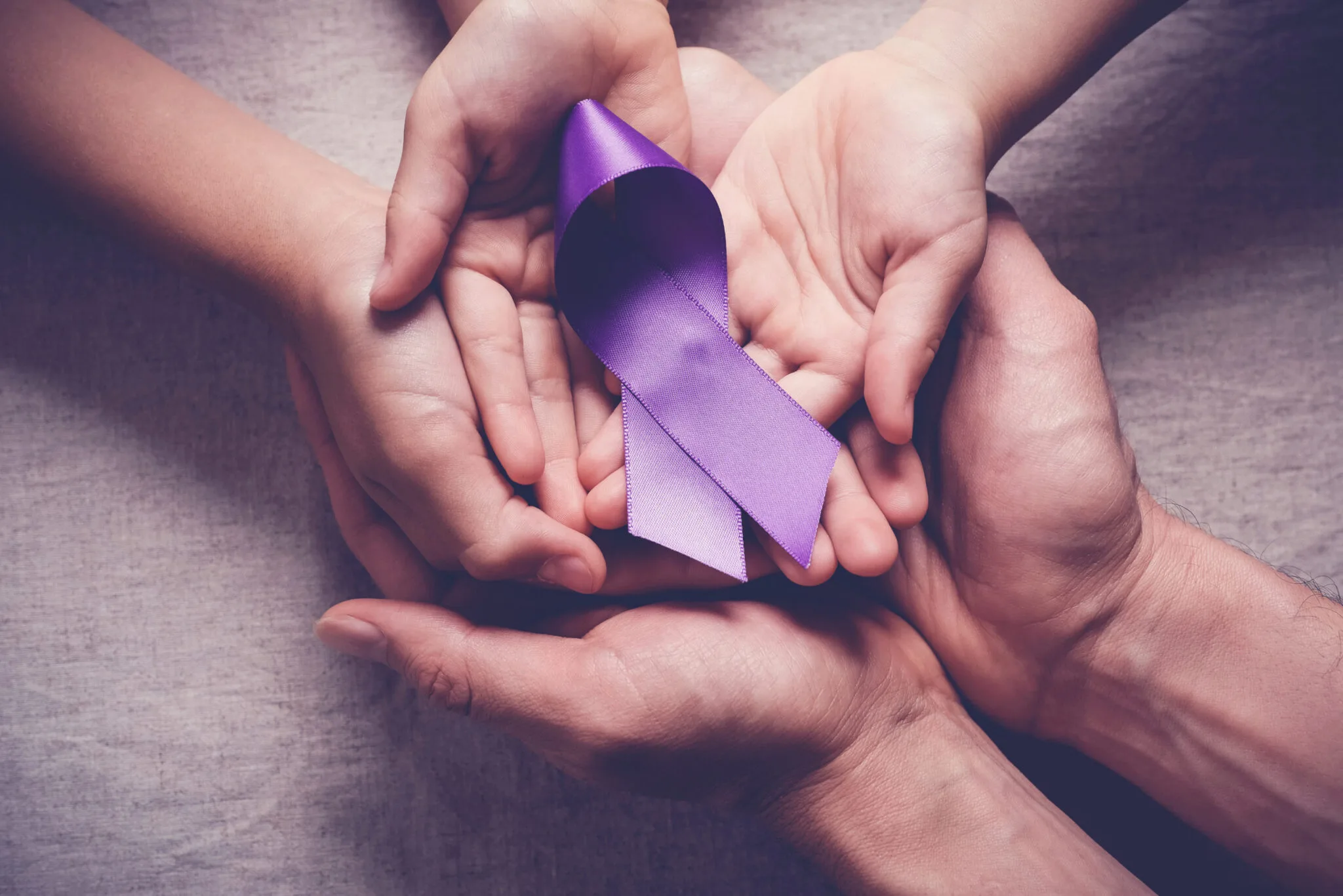 May show: Three pairs of hands hold a purple awareness ribbon together, symbolizing support and unity.